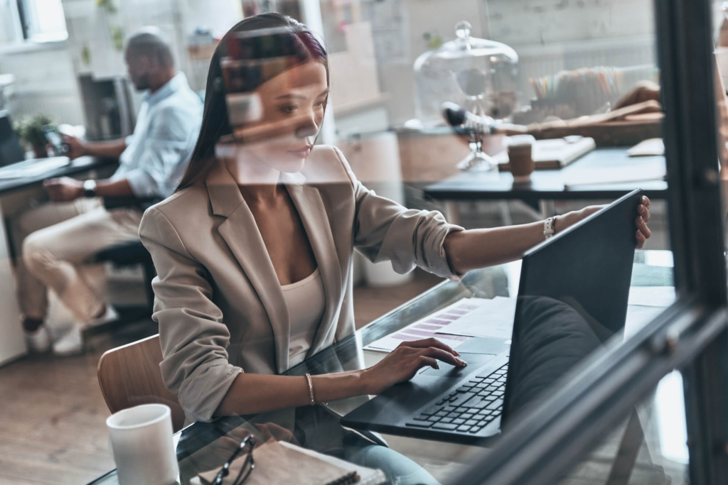 Ambiente de escritório moderno e iluminado, com três pessoas trabalhando em seus respectivos laptops