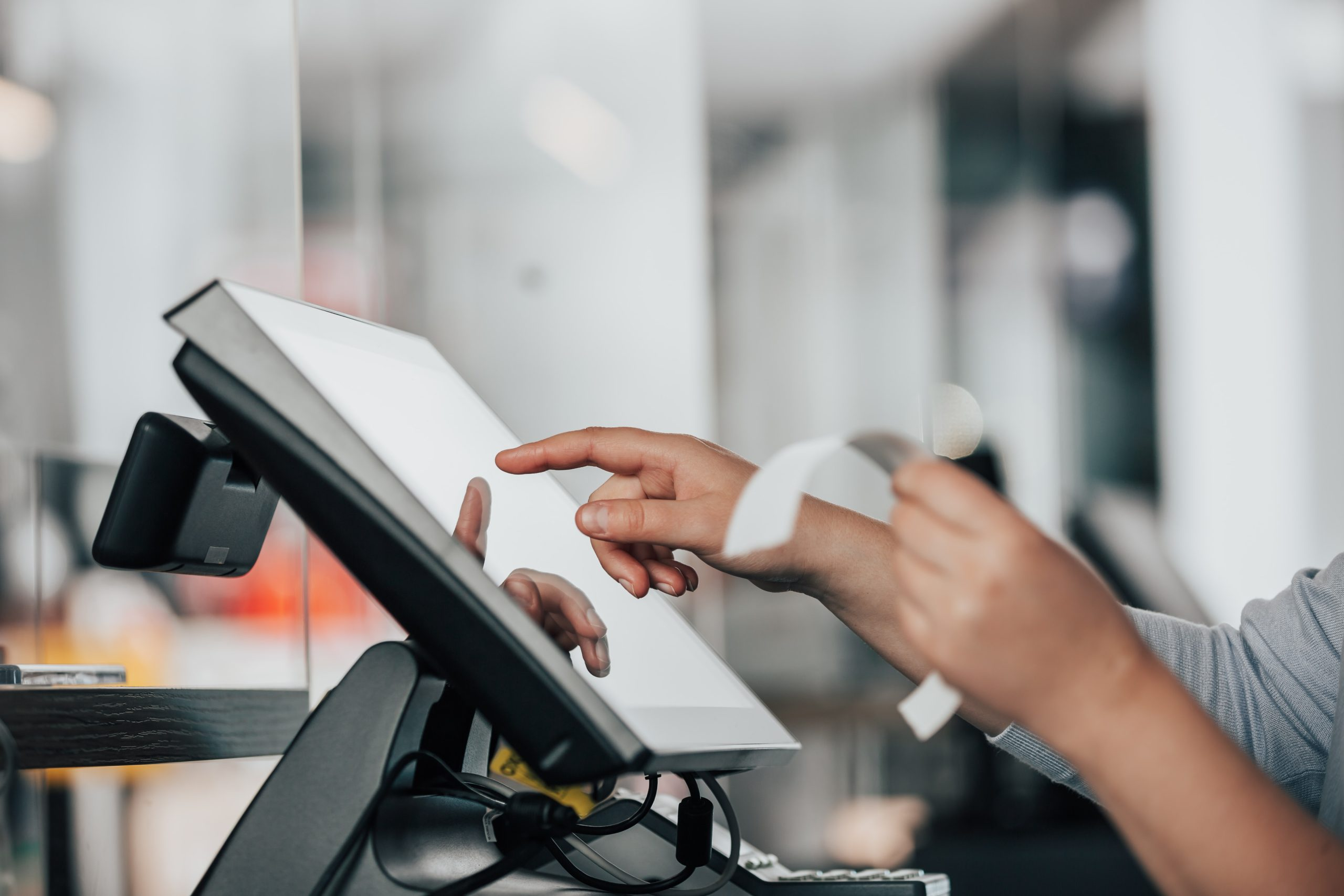 Pessoa interagindo com uma tela touch, usando um dispositivo de pagamento enquanto segura um recibo. Representa uma nota fiscal de estorno.